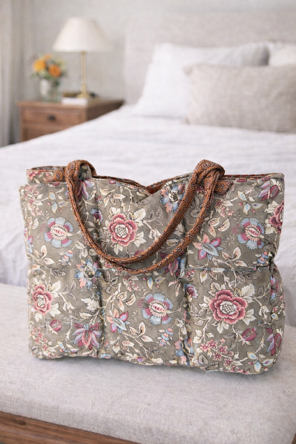 Floral-patterned bag on a bed with a lamp and flowers in the background
