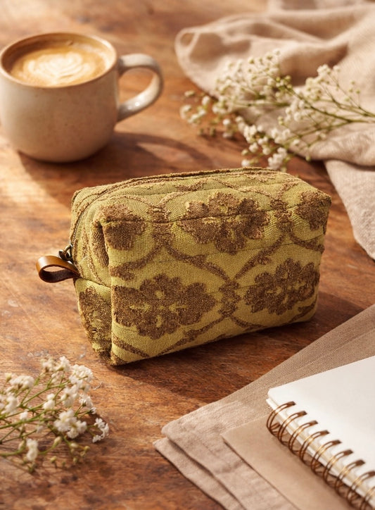 Green patterned pouch on a wooden surface with a cup of coffee and flowers.