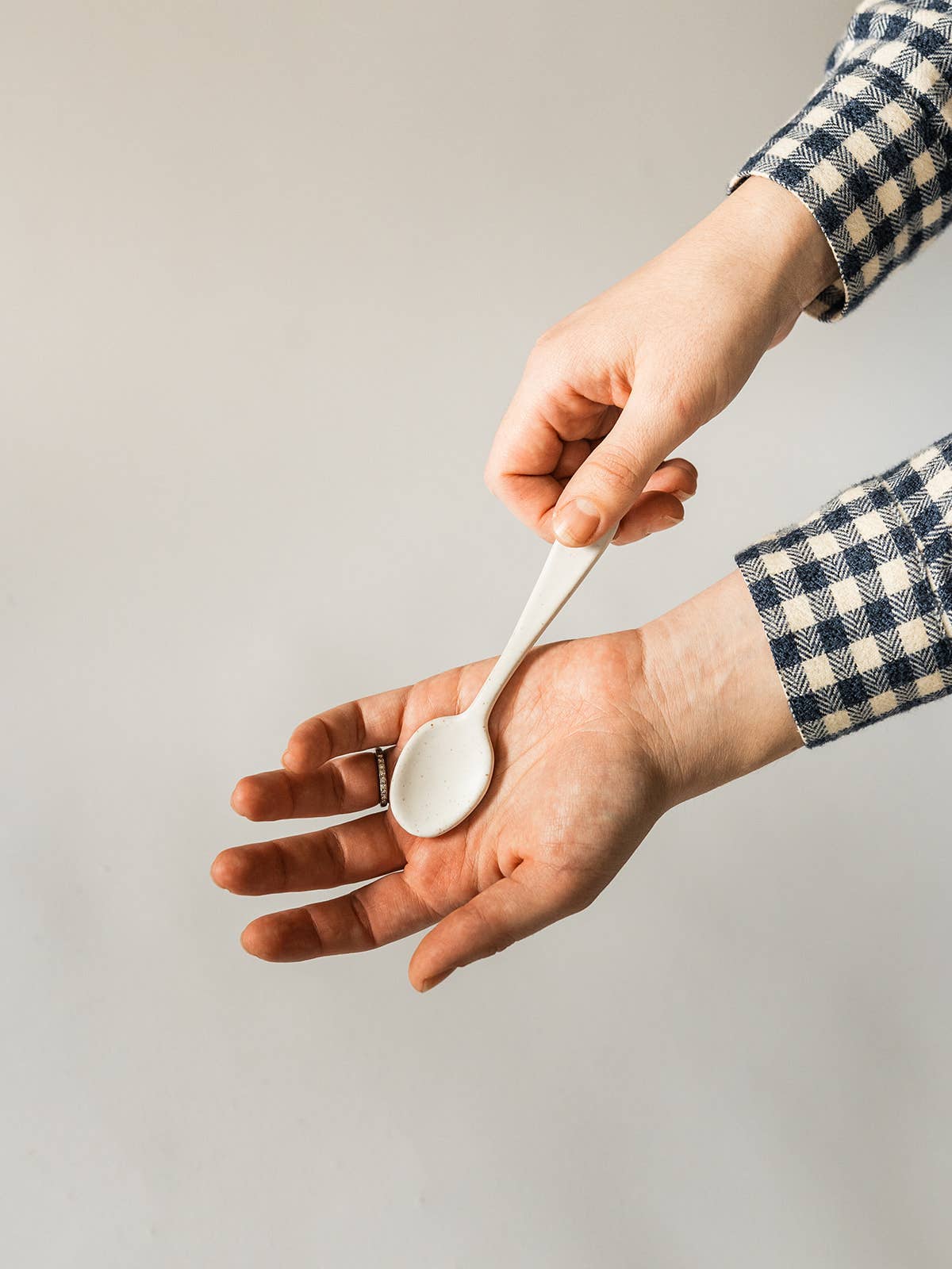 Person holding a white spoon with a neutral background