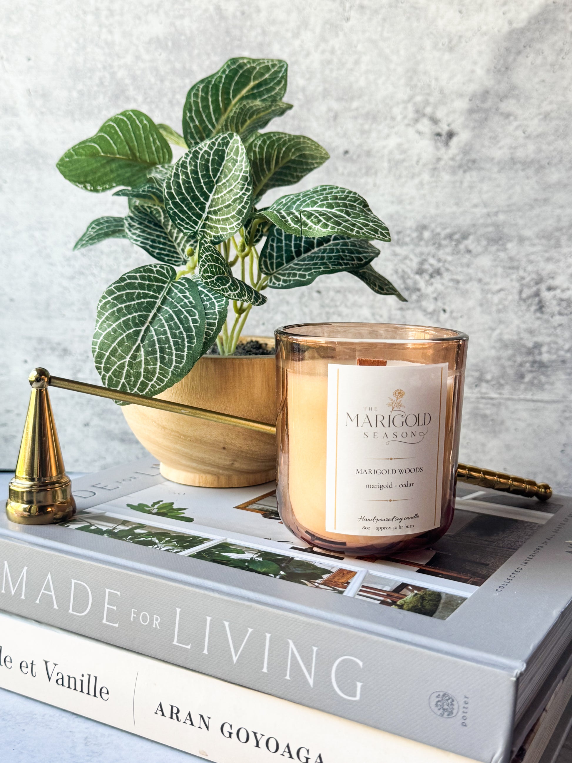 Marigold Woods candle in amber glass styled on design books with a plant and brass accents for an elevated home fragrance product photo.