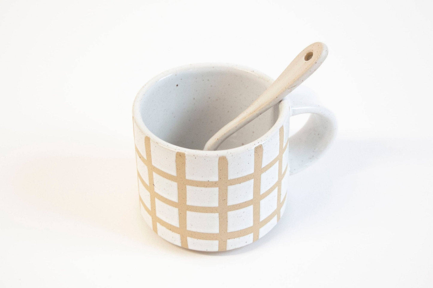 White mug with beige grid pattern and wooden spoon on a white background