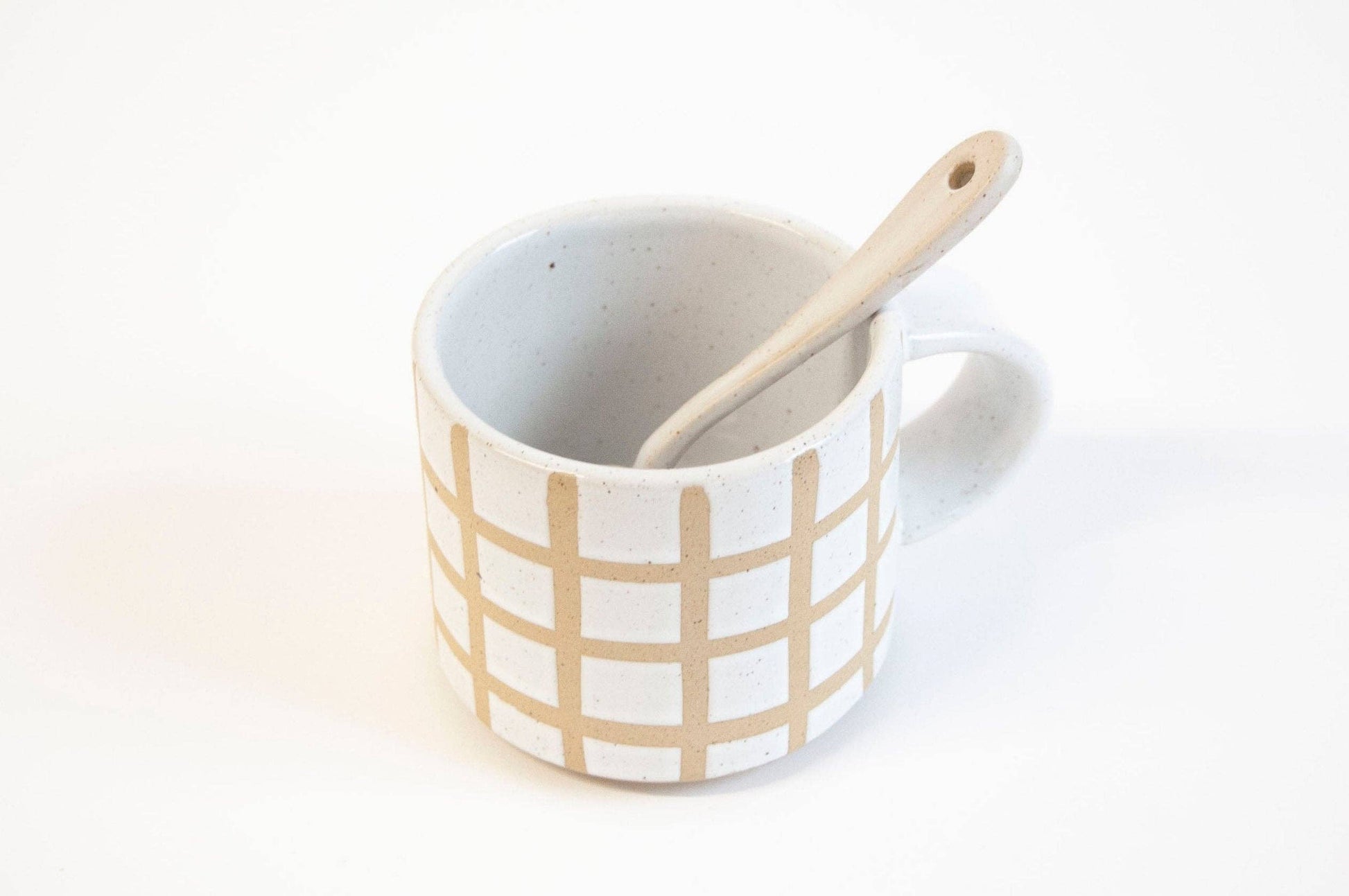 White mug with beige grid pattern and wooden spoon on a white background