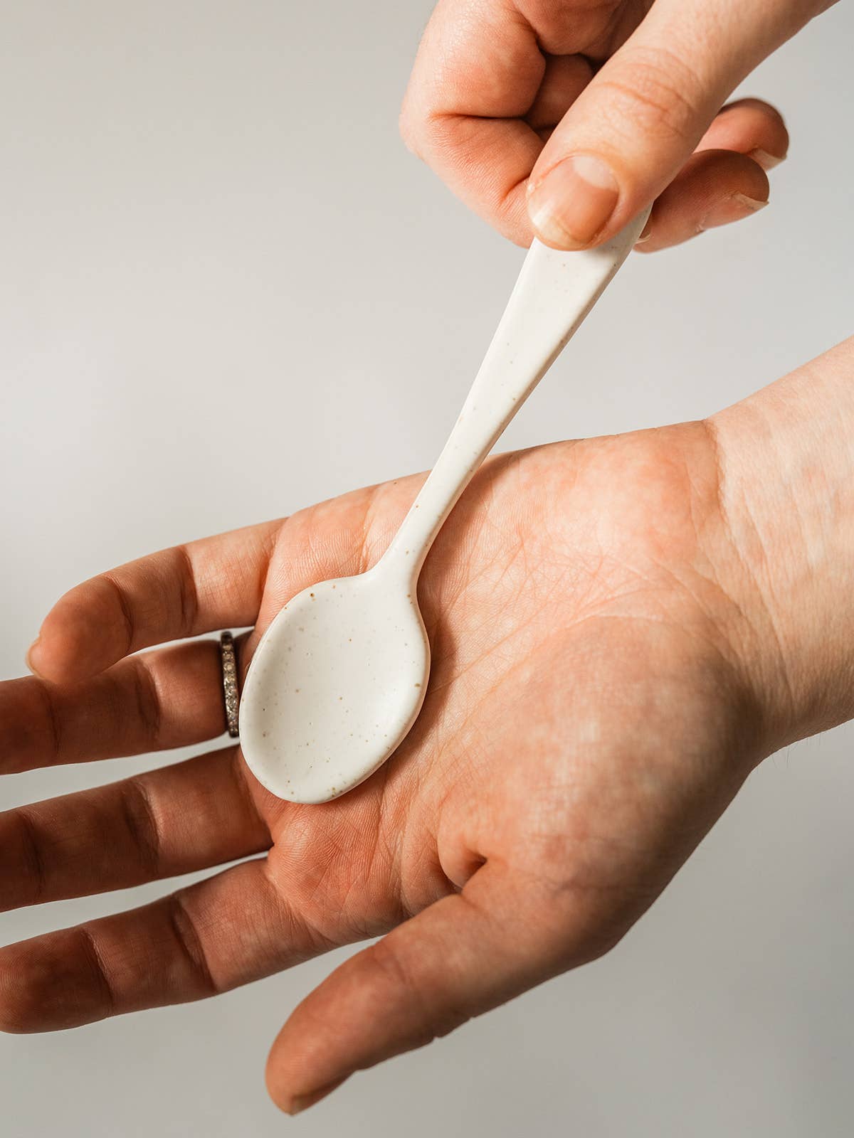 Person holding a small ceramic spoon between their hands against a neutral background