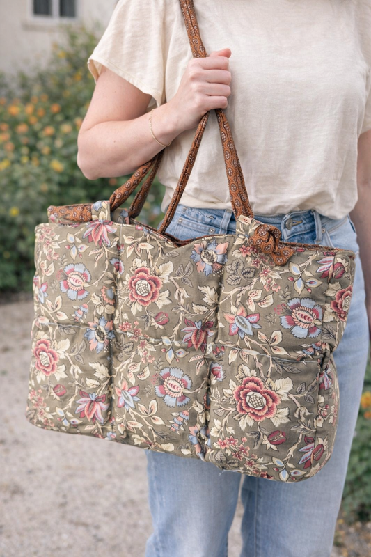 Person holding a floral quilted tote with a brown strap outdoors.