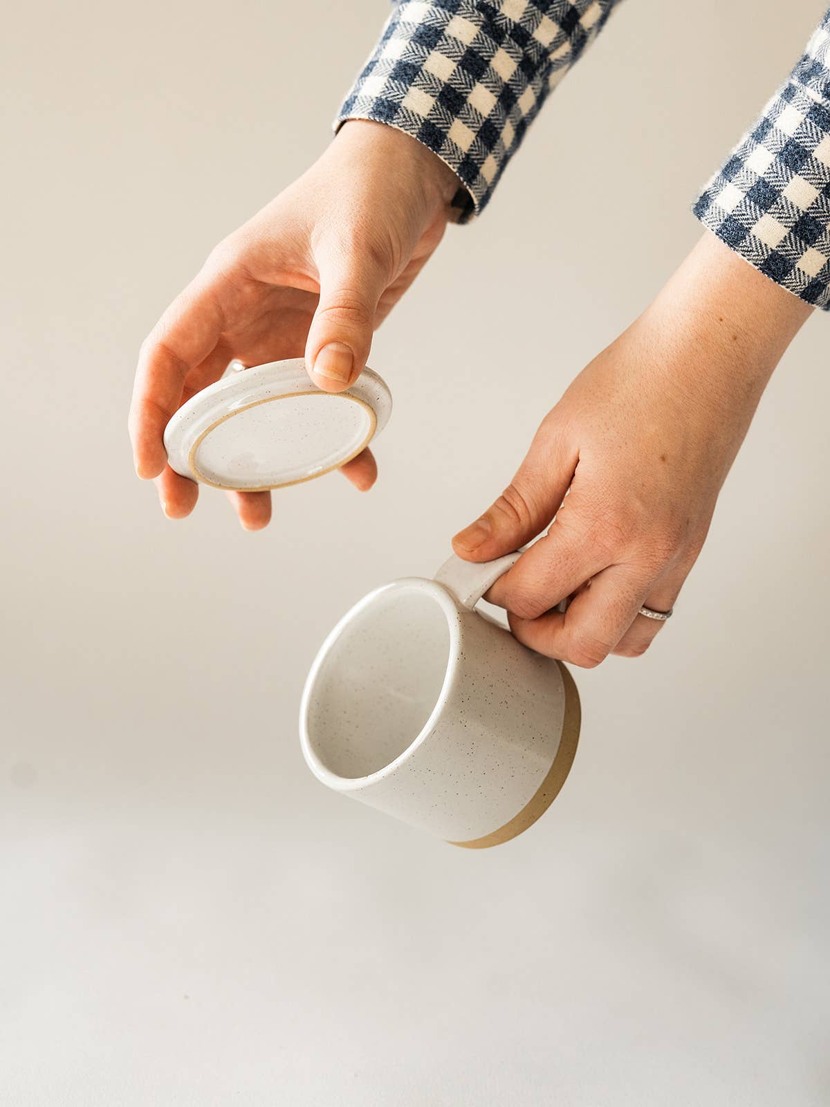 Person holding a white ceramic mug and its lid on a light background