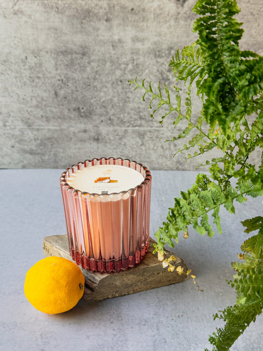 Blush ribbed glass Lemon & Lilac candle styled on a stone slab with a lemon and green fern for a fresh spring home fragrance product photo.