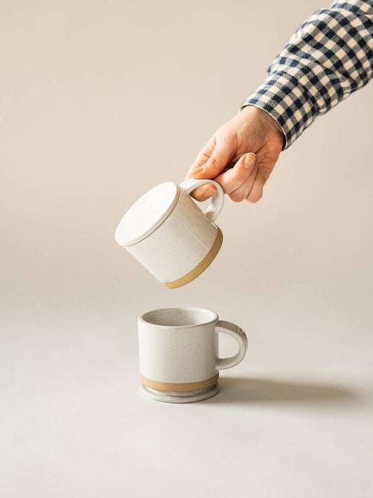 Person holding a white mug with a beige interior against a plain background