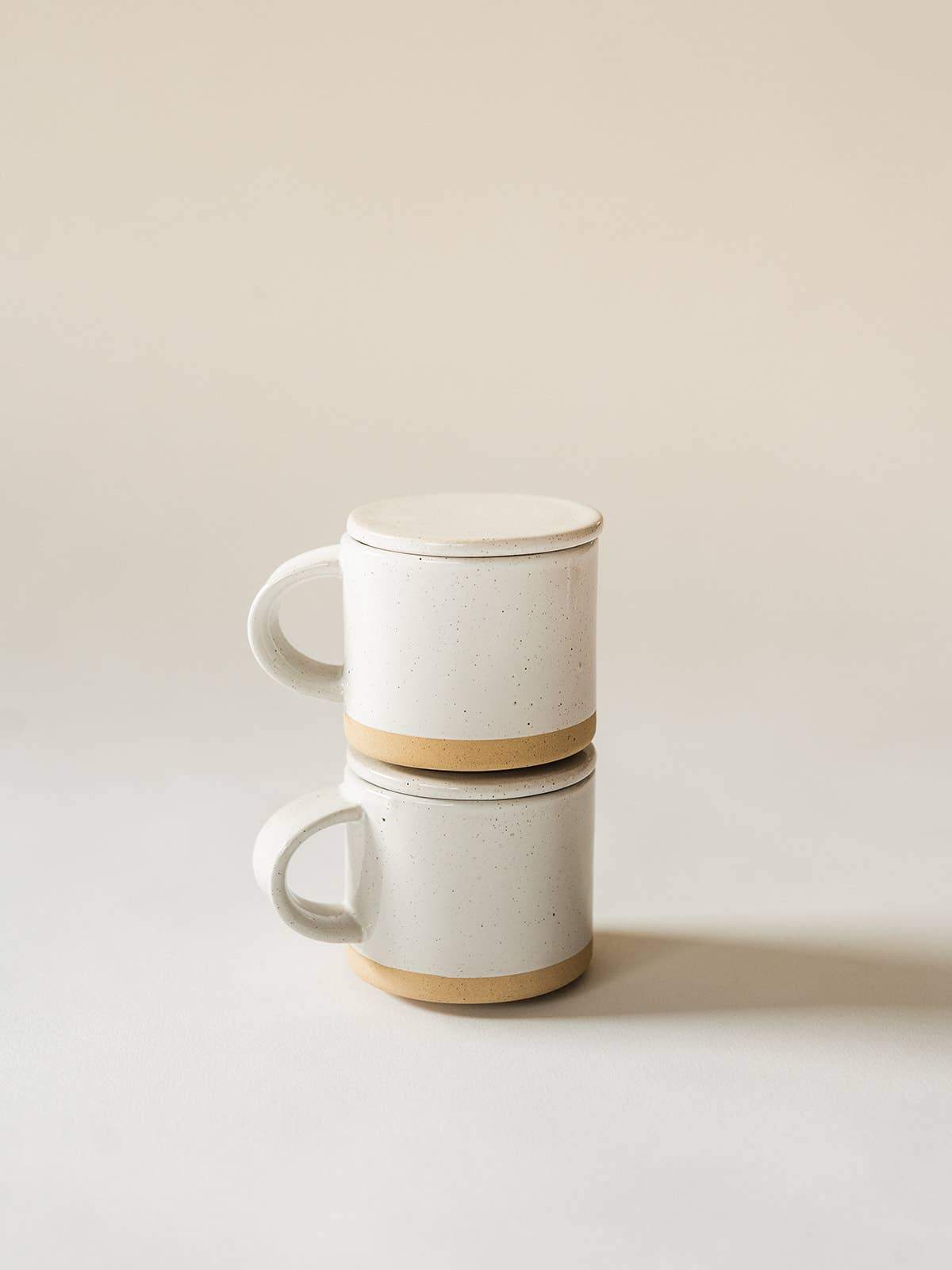 Two ceramic mugs stacked on a light beige background