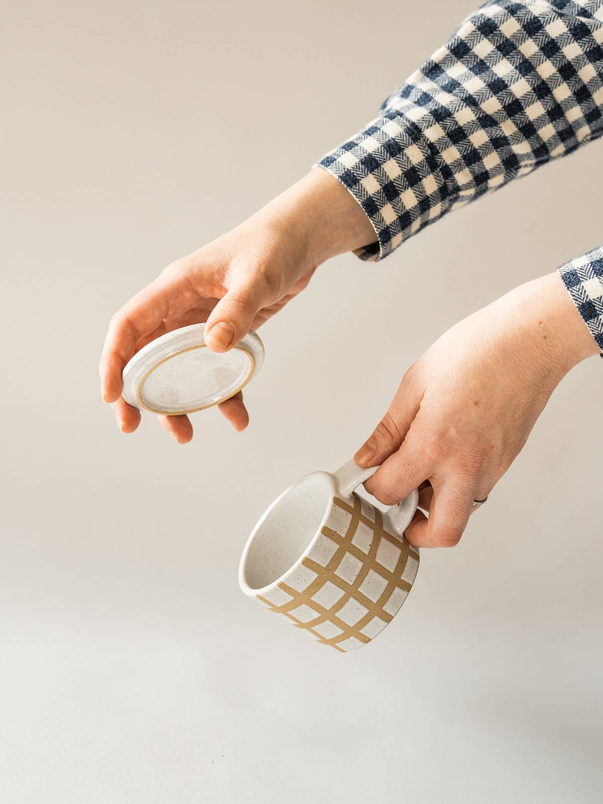 Person holding a white mug with gold grid pattern and a matching lid on a light background